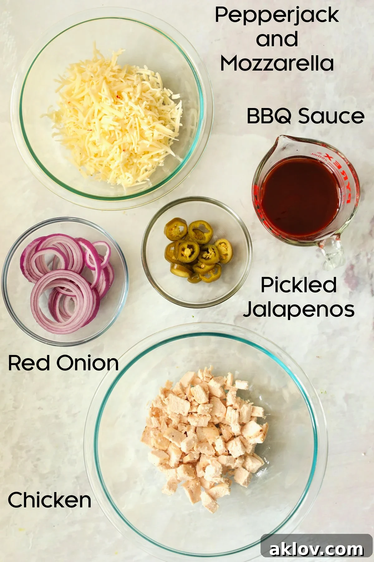 Assortment of prepped Cast Iron Skillet Pizza ingredients in glass bowls: barbecue sauce, shredded cheeses, diced chicken, red onion, and pickled jalapenos.