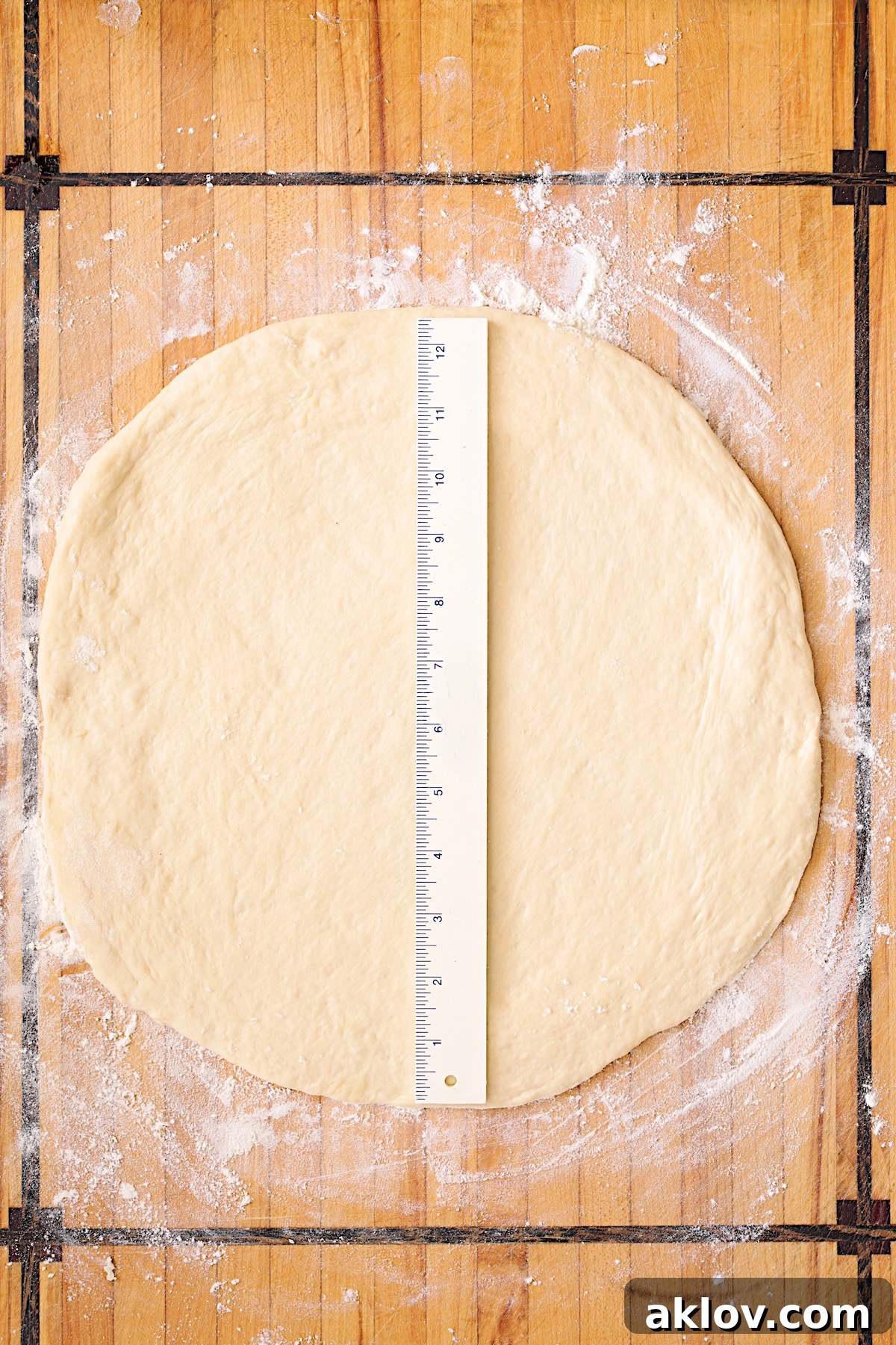 Rolled out pizza dough on wood cutting board with ruler on it to demonstrate the size.