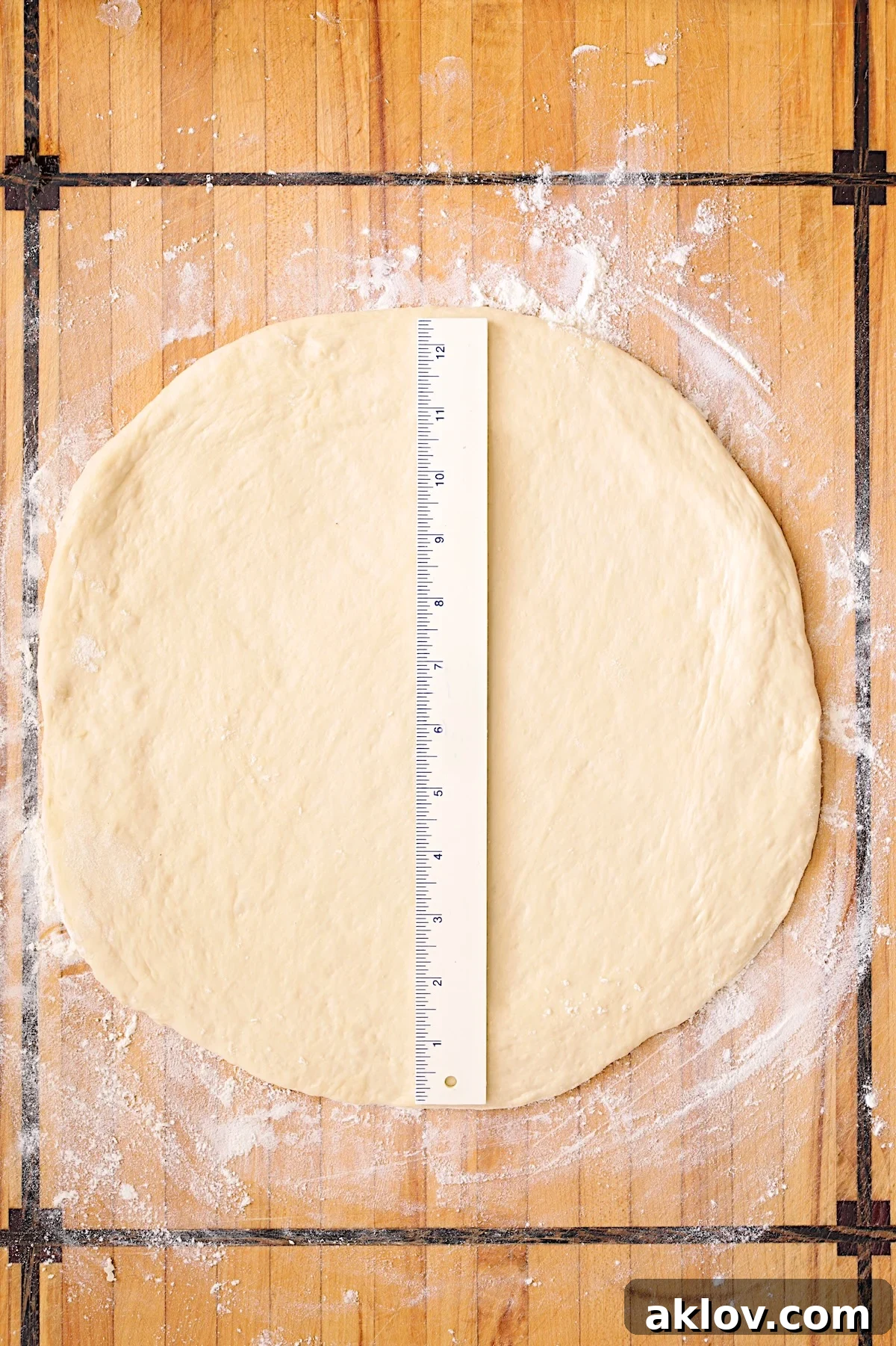 Pizza dough rolled out into a 12-inch circle on a wooden cutting board, with a ruler demonstrating its size.