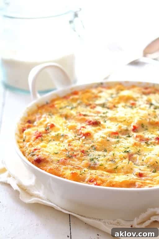The finished Spicy Shrimp and Grits Casserole with Gouda Cheese, baked golden brown in a white oval baking dish, resting on a rustic white wooden background, ready to be served.