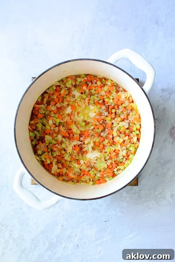 Photo of onion, carrot, garlic and celery being sautéed in white Dutch oven.