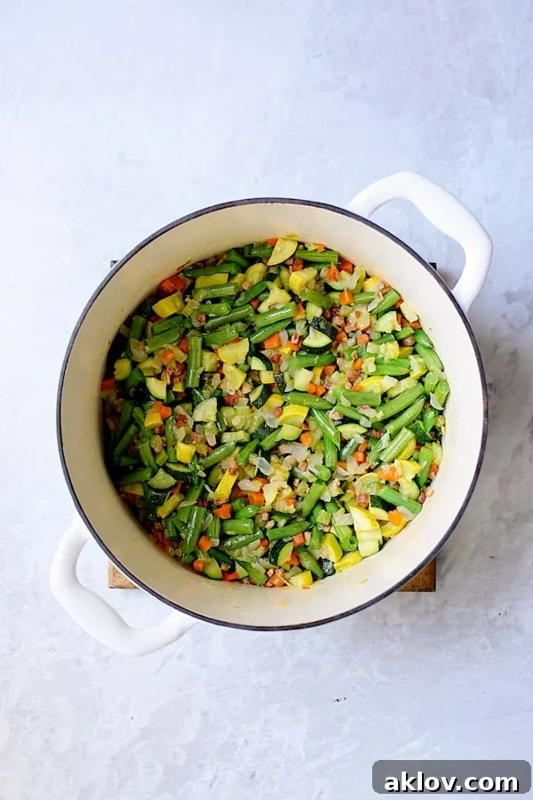 Photo with zucchini, yellow squash and green beans added to the cooking aromatics in white Dutch oven.