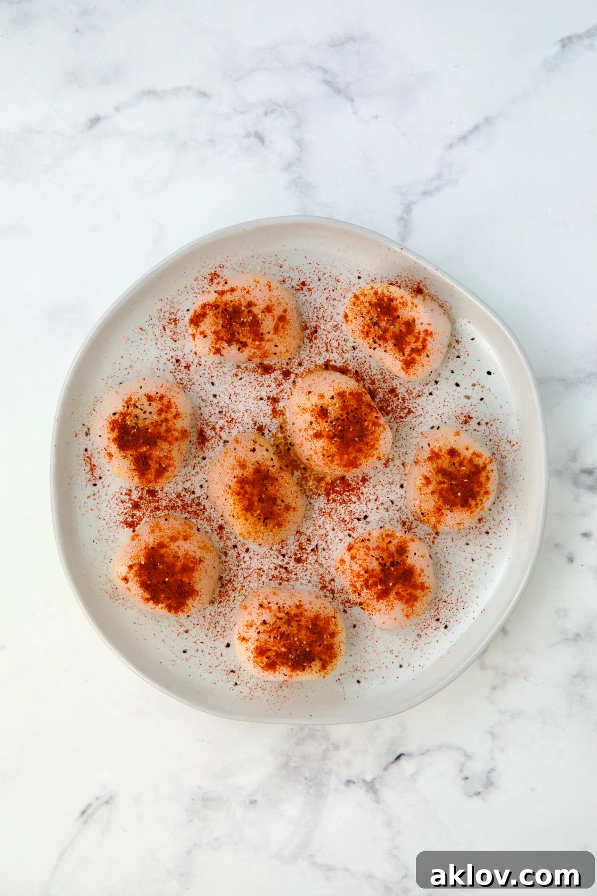 Uncooked seasoned sea scallops on white plate.