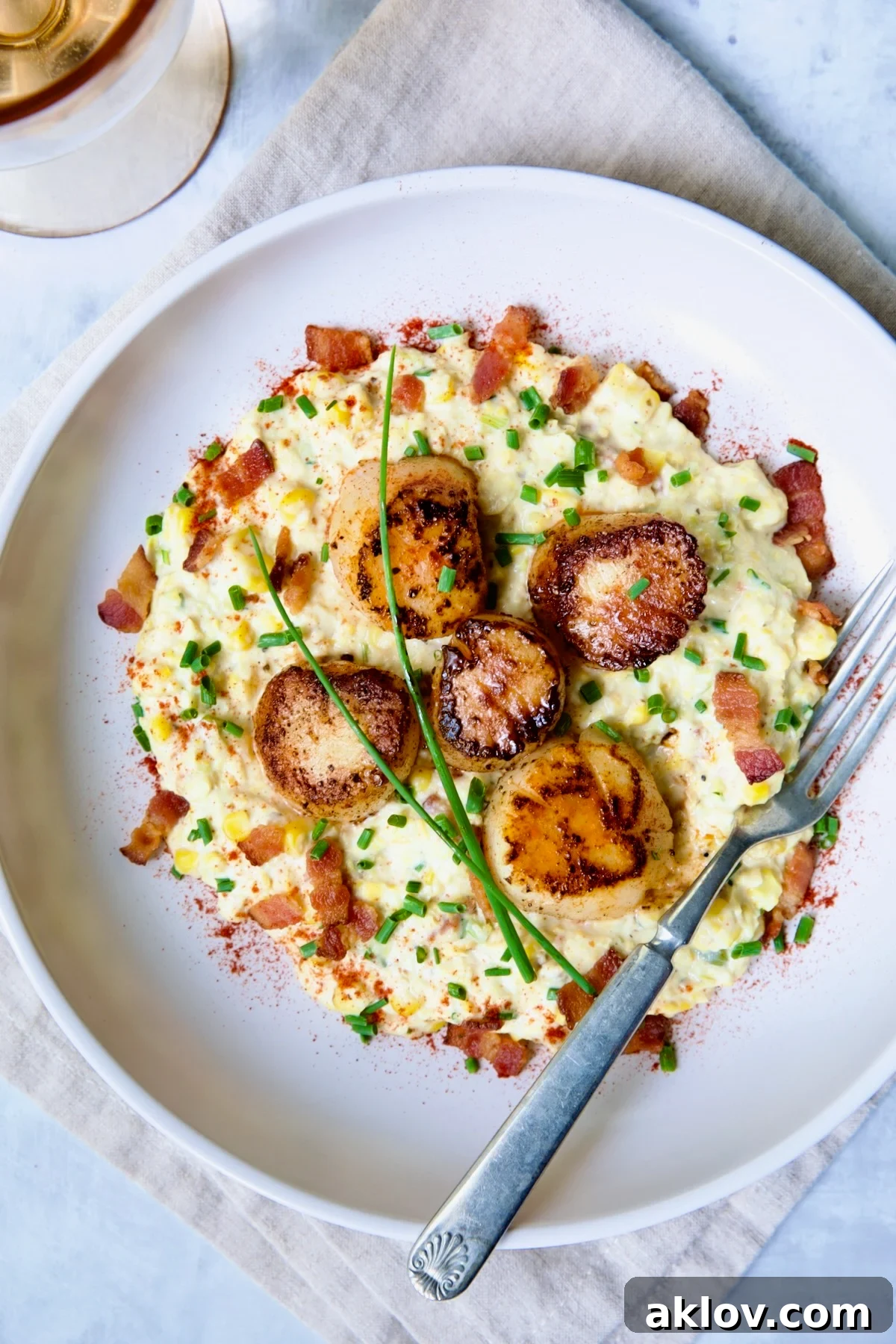 One serving of Seared Sea Scallops with Smoky Sweet Corn Puree on white plate with fork garnished with fresh chives.