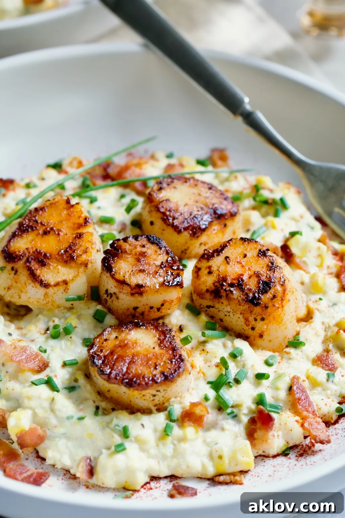 One serving of Seared Sea Scallops with Smoky Sweet Corn Puree on white plate with fork.