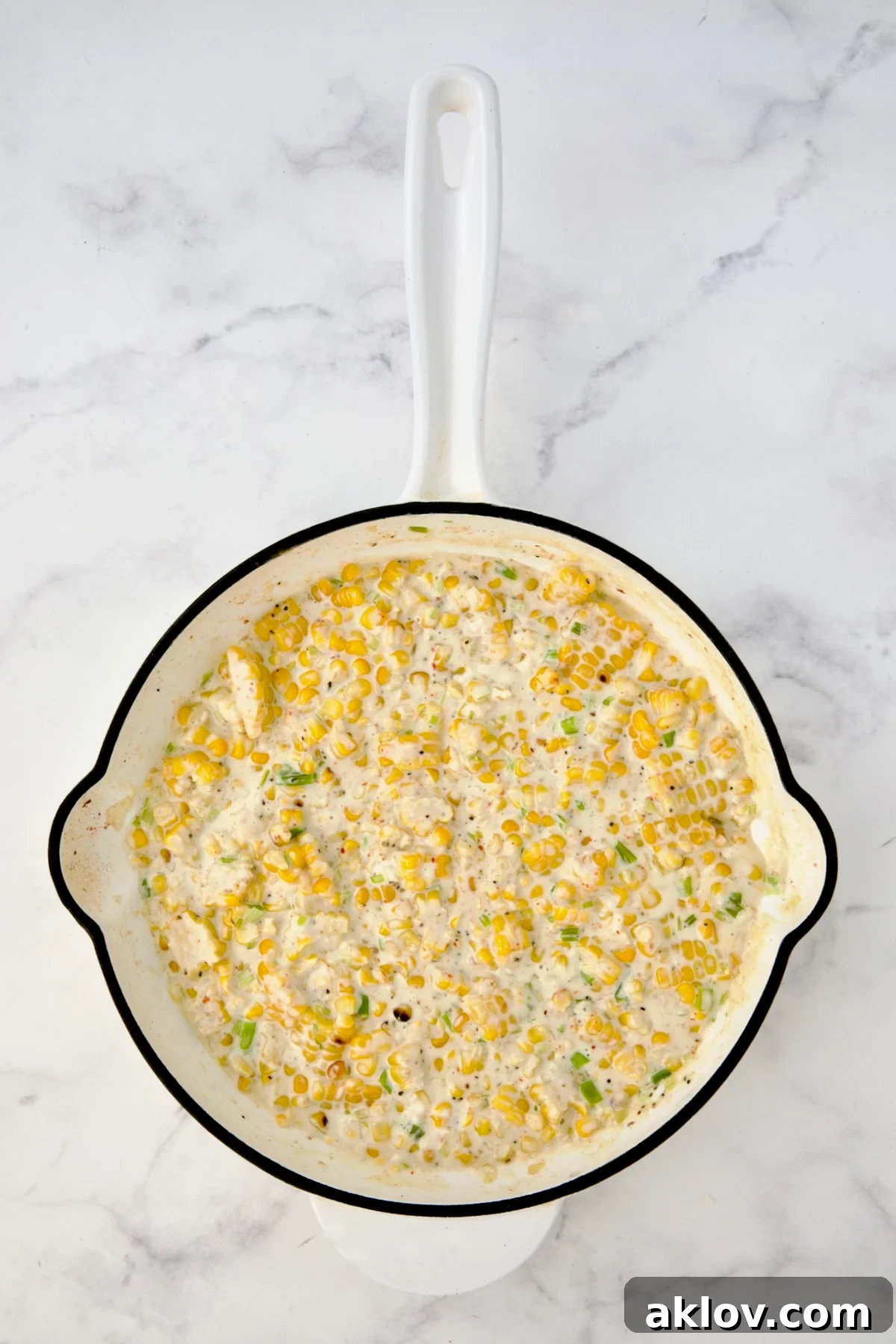 Cream cheese and heavy cream added to corn in white enamel cast iron skillet after being stirred in.