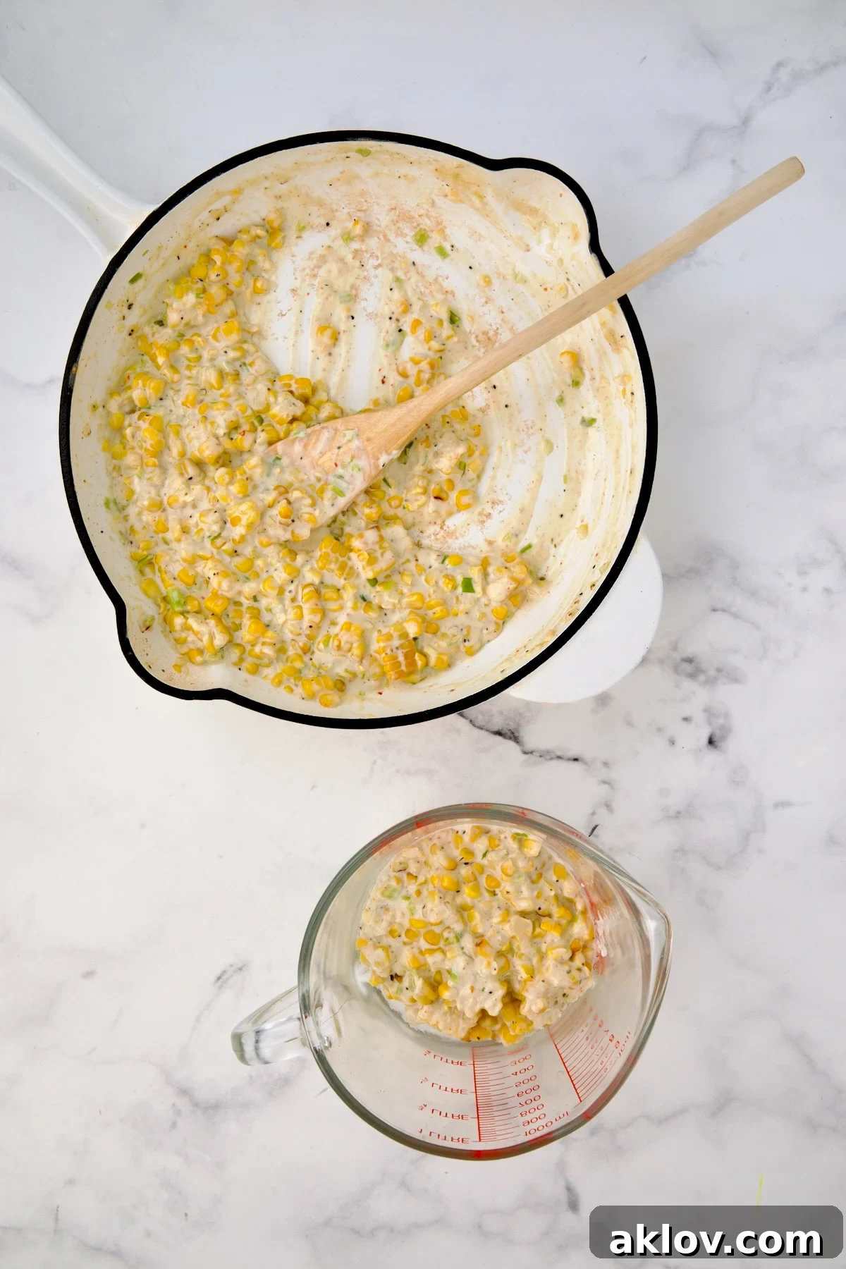 Creamy corn combination in white enamel cast iroon skillet with some placed in a glass measuring cup.