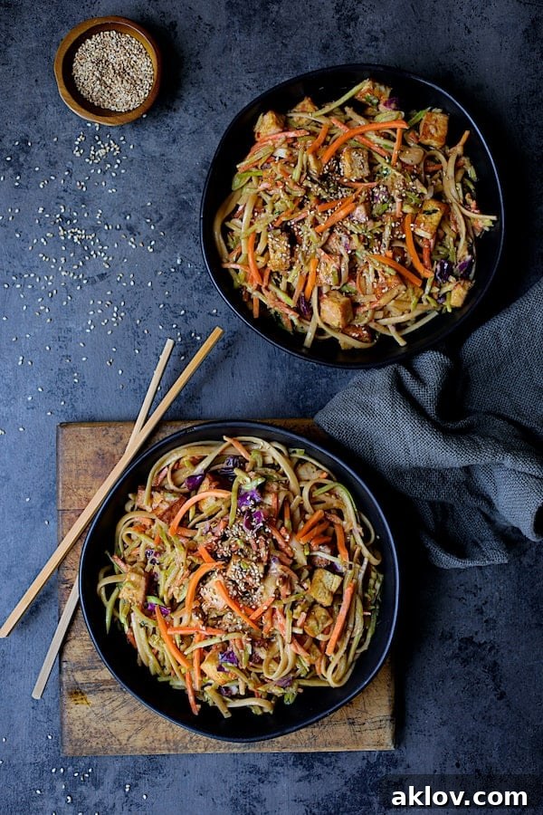 Thai Sesame Noodles with Tofu and Vegetables - Overhead shot of noodles in black bowls on dark blue background with chopsticks and gray napkin