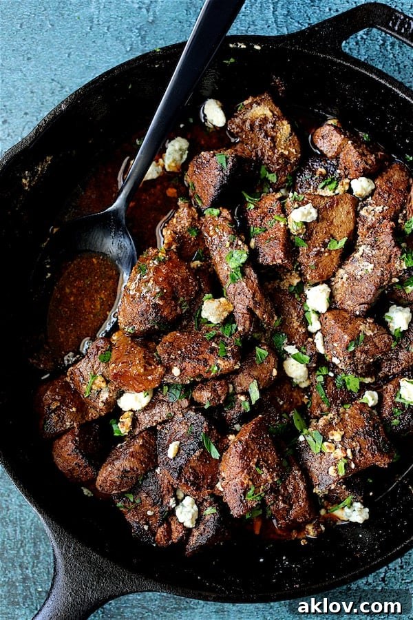 Crumbled Gorgonzola cheese being added over the Buttery Blackened Steak Bites in a cast iron skillet.