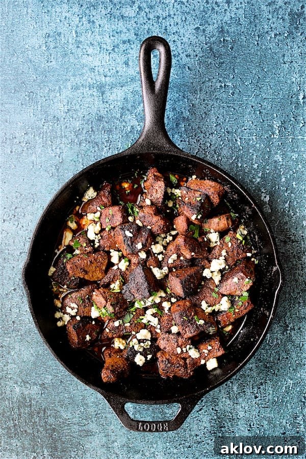 Overhead shot of Buttery Blackened Steak Bites in a cast iron skillet, with crumbled Gorgonzola cheese sprinkled over them.