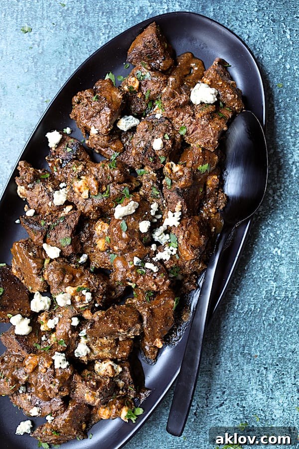 Close-up shot of Buttery Blackened Steak Bites on a black platter, garnished with more Gorgonzola cheese and fresh parsley.