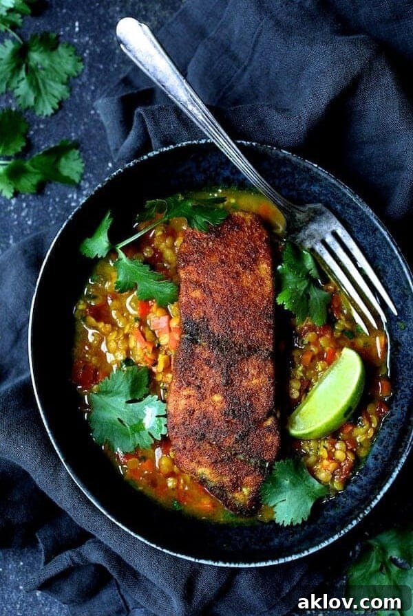 Indian Spiced Sea Bass with Braised Red Lentils in black bowl with fork, cilantro sprigs and lime wedges.