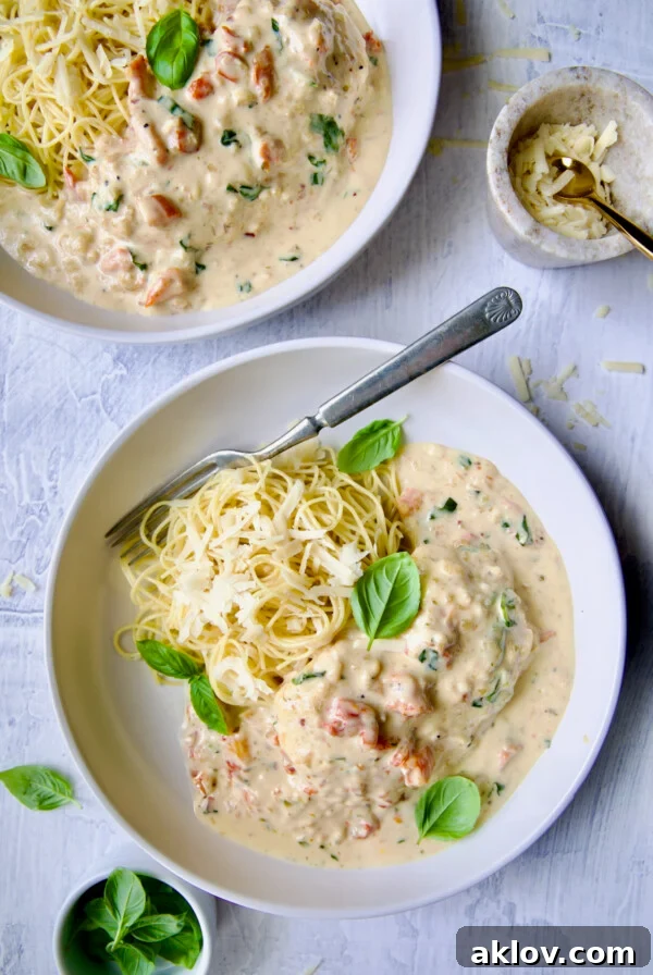 Marry Me Chicken in white bowl with angel hair pasta and fork garnished with fresh basil leaves.