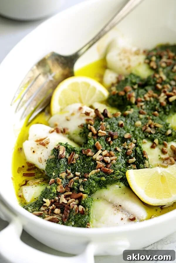 Baked Tilapia with Spinach Pecan Pesto - Straight-on close-up shot of finished dish garnished with chopped pecans and lemon wedges