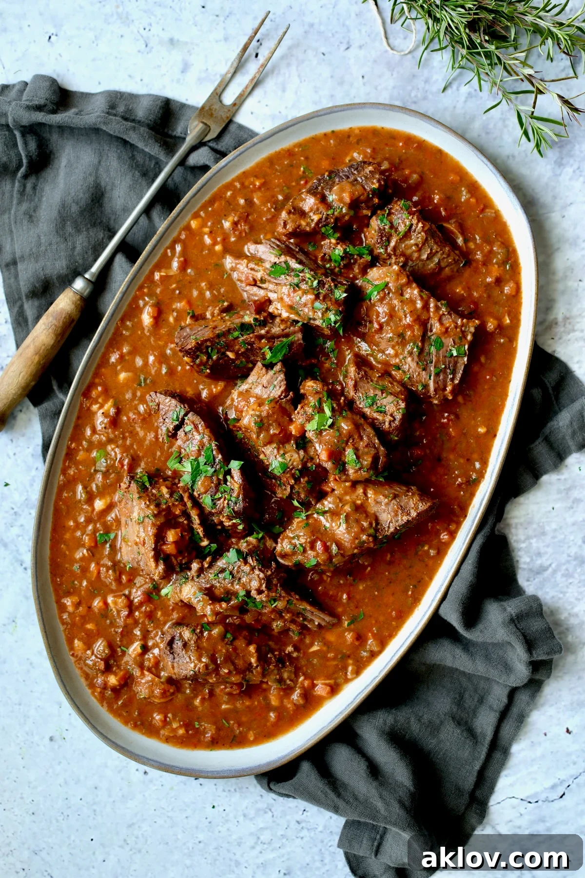 Italian Pot Roast (Stracotto) broken into pieces on oval gray-rimmed platter with meat fork.