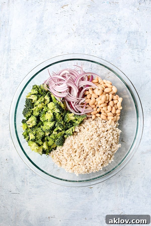 Selected ingredients for Lemony Broccoli, Barley, and White Bean Salad in a large glass mixing bowl.