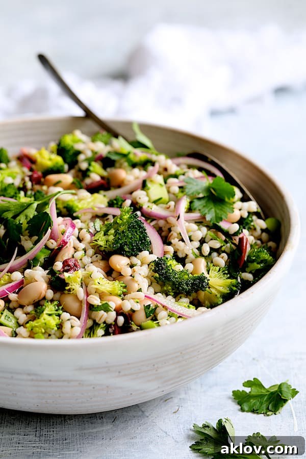 Close-up shot of Lemony Broccoli, Barley, and White Bean Salad in a white serving bowl with a serving spoon, showing detailed texture.