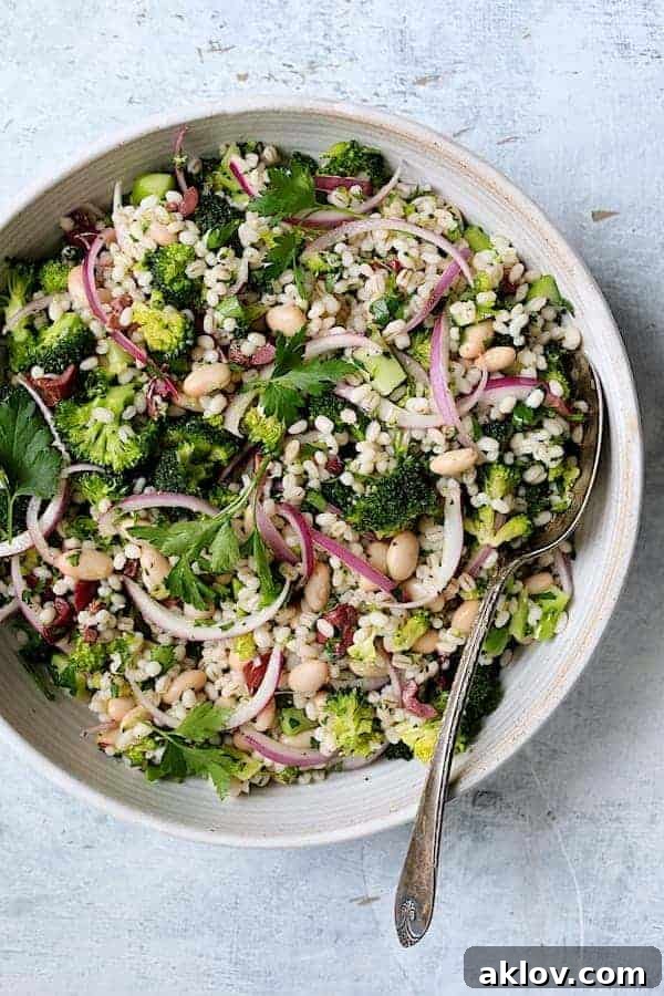 Full view of Lemony Broccoli, Barley, and White Bean Salad in a white serving bowl with a serving spoon.