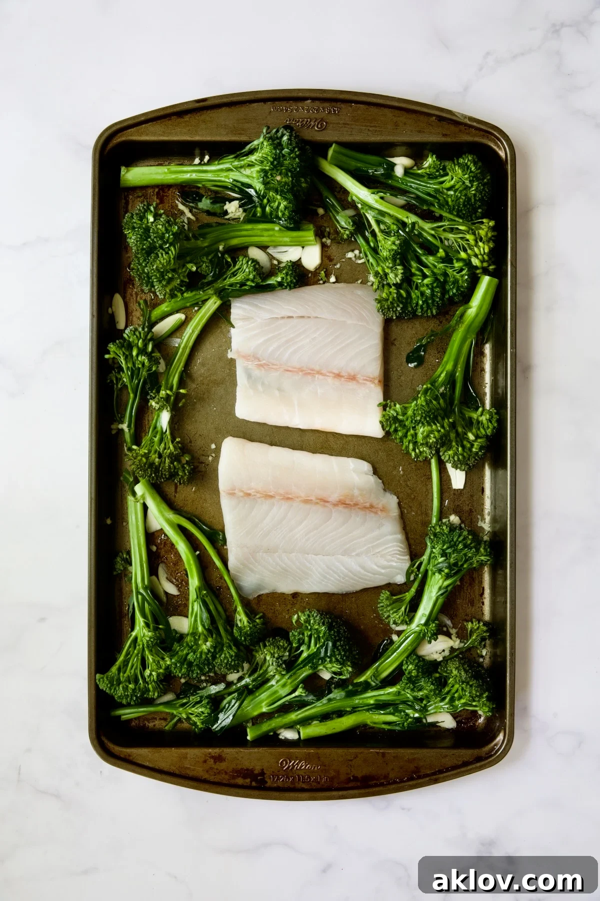 Broccolini and two pieces of fish on rimmed sheet pan.