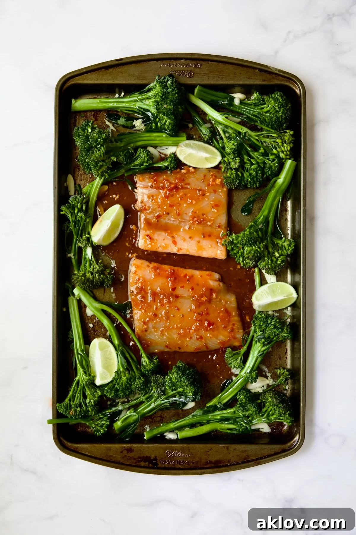 Broccolini and two pieces of fish with glaze poured over on rimmed sheet pan.