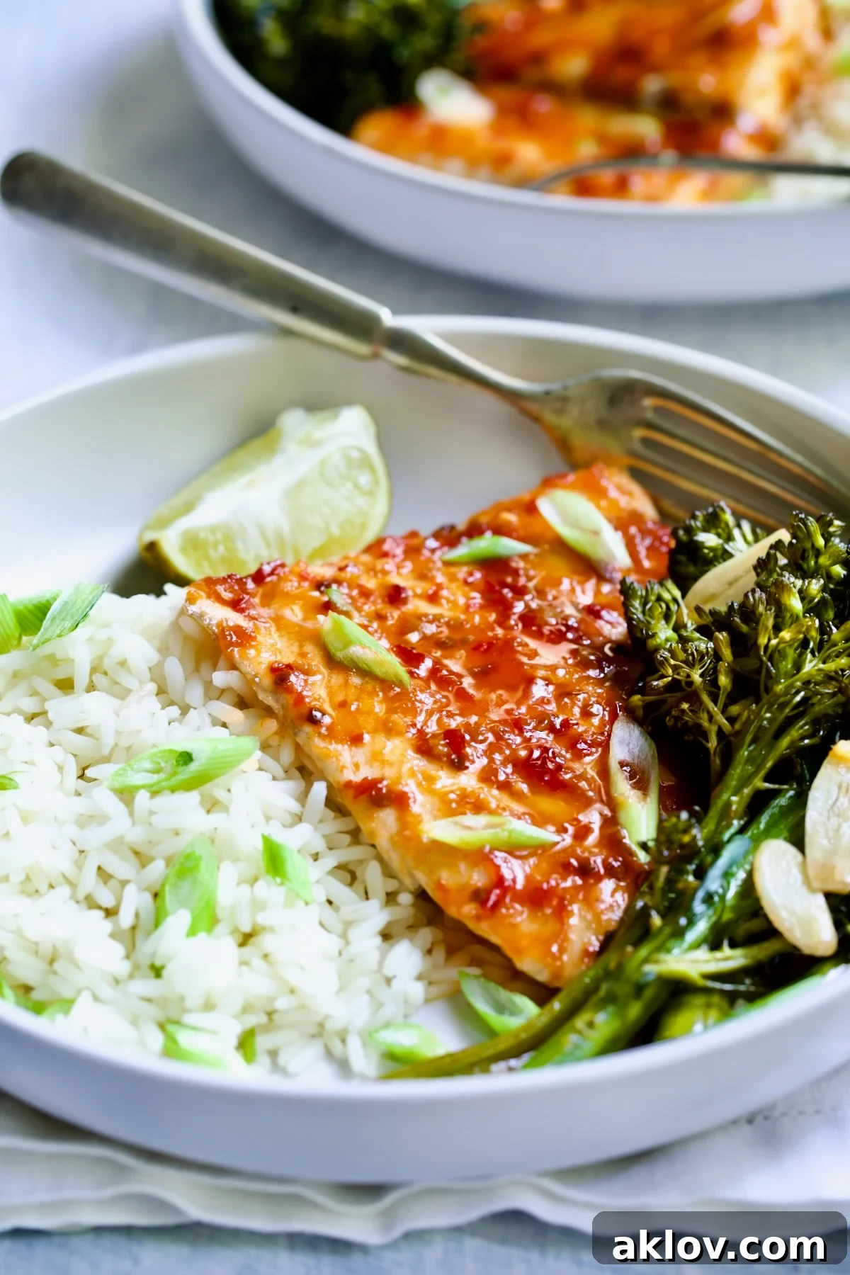 Sheet Pan Thai Baked Fish with Broccolini on white plate with fork and lime wedge.