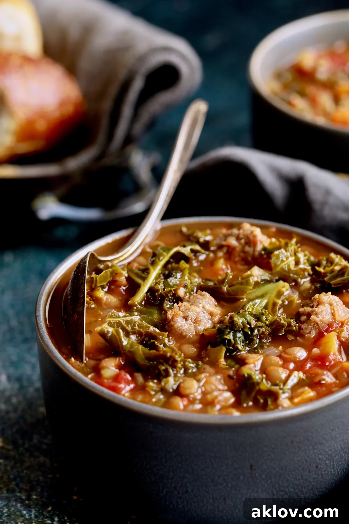 Sausage and Lentil Soup with Kale served in a gray bowl, with a spoon resting on the edge, inviting a taste.