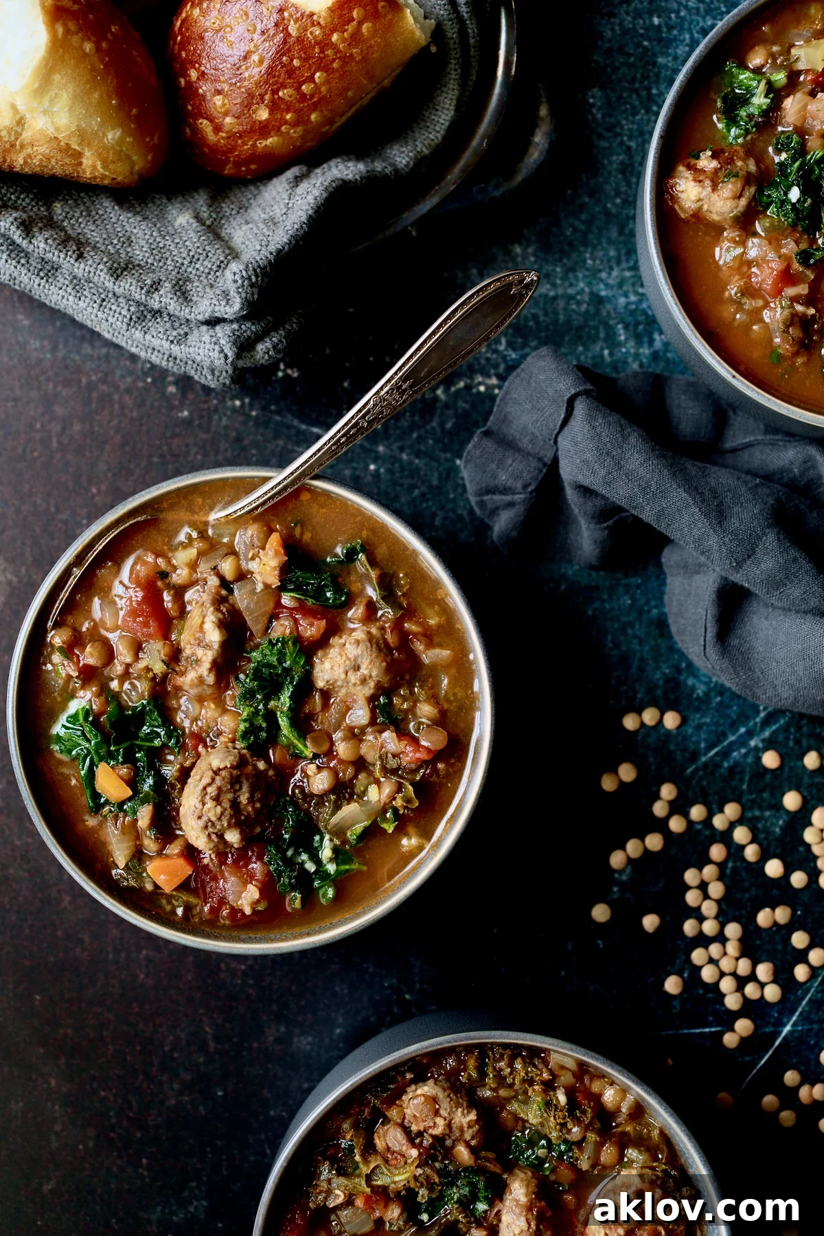 A single bowl of vibrant Sausage and Lentil Soup with Kale, set on a gray napkin, with loose lentils scattered around, highlighting its rustic appeal.