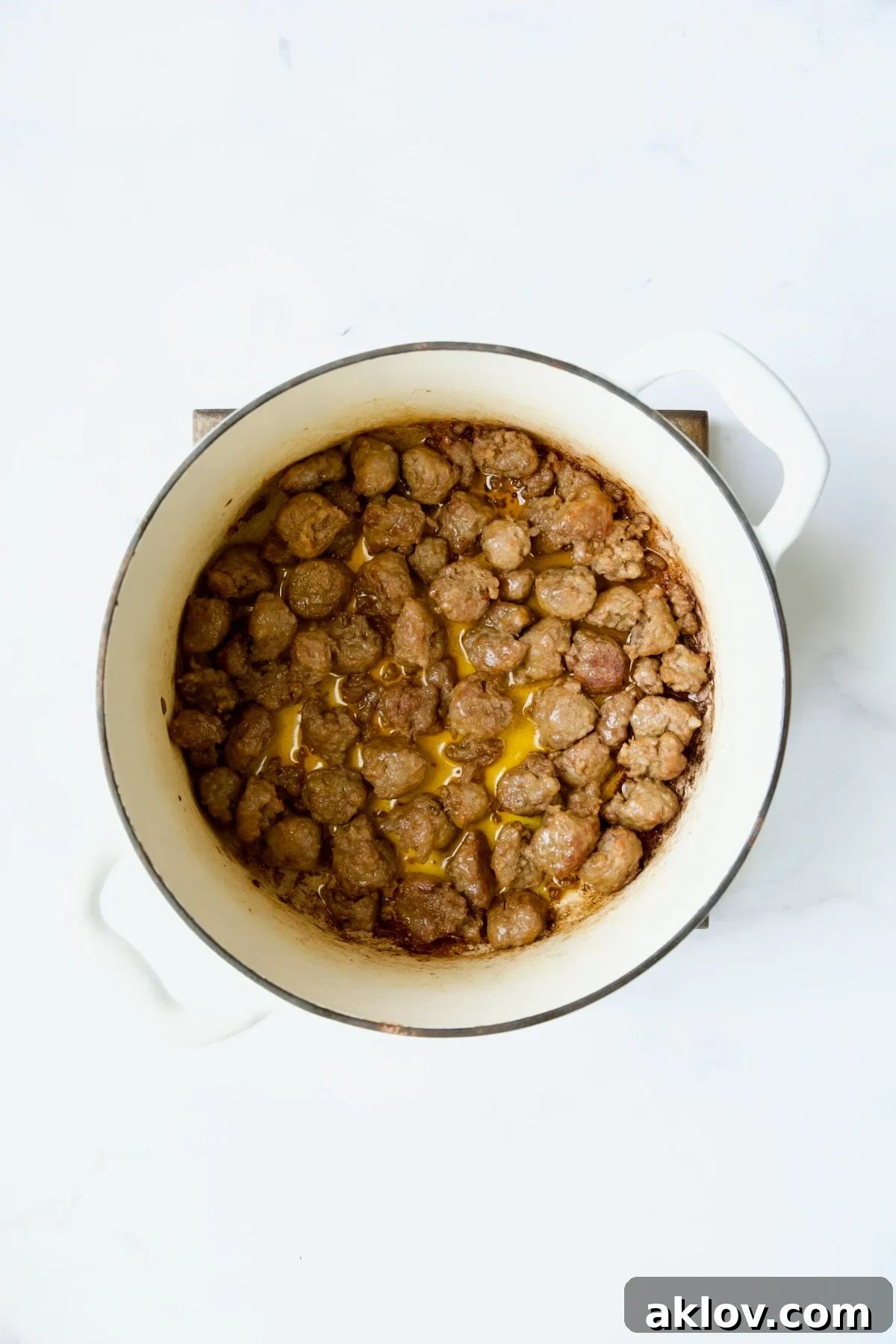 Cooked Italian sausage pieces in a white Dutch oven, showing the browning process.
