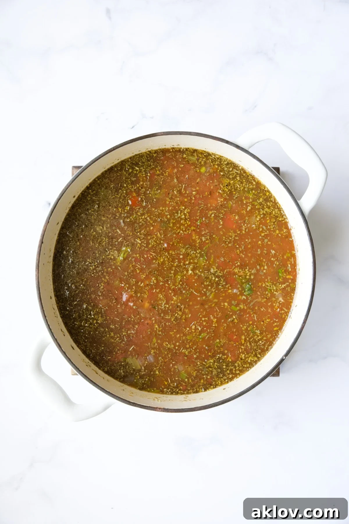All the main ingredients for Sausage and Lentil Soup with Kale assembled in a white Dutch oven before cooking, showcasing the broth, tomatoes, and sausage.