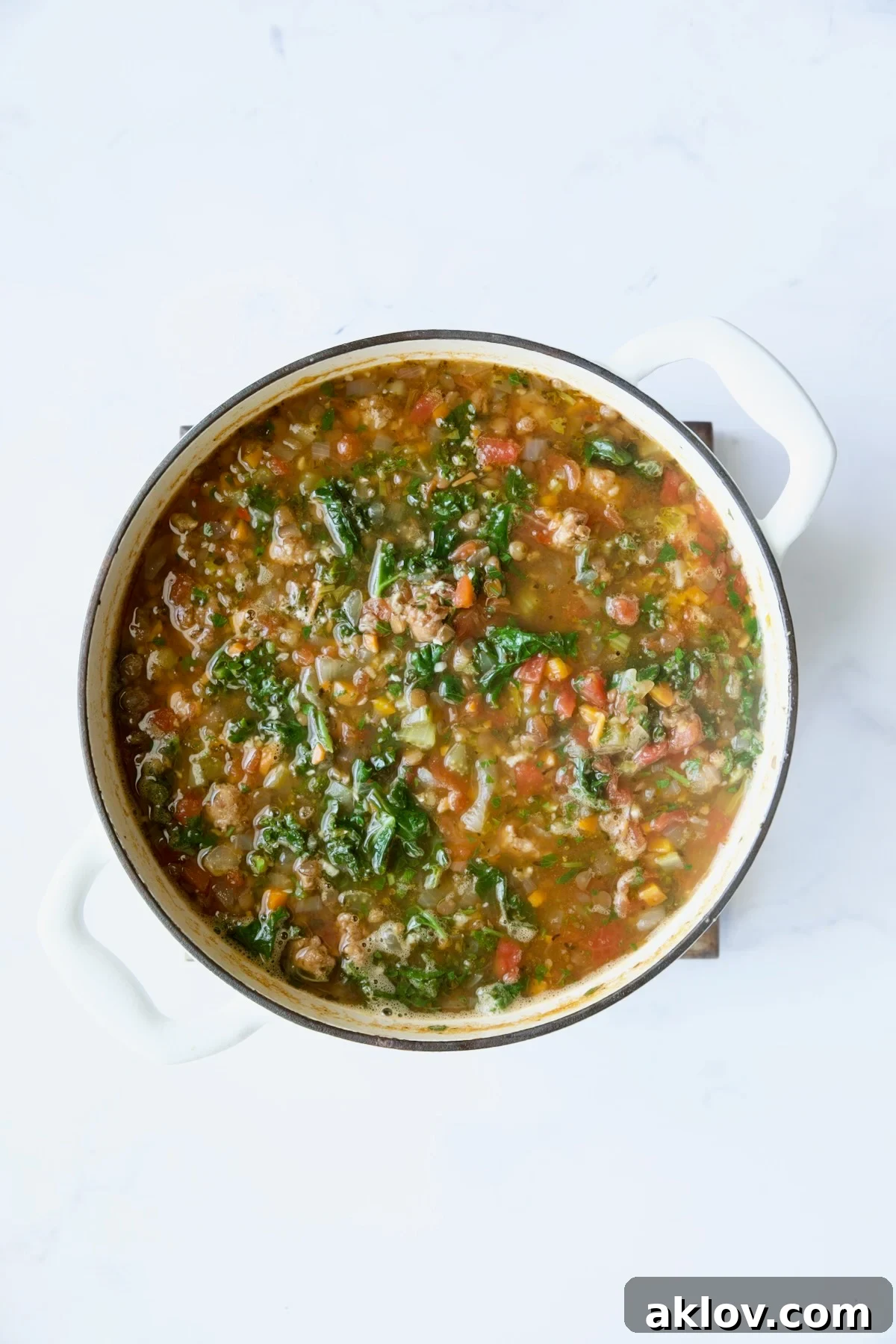 The finished Sausage and Lentil Soup with Kale, richly colored and simmering in a white Dutch oven.