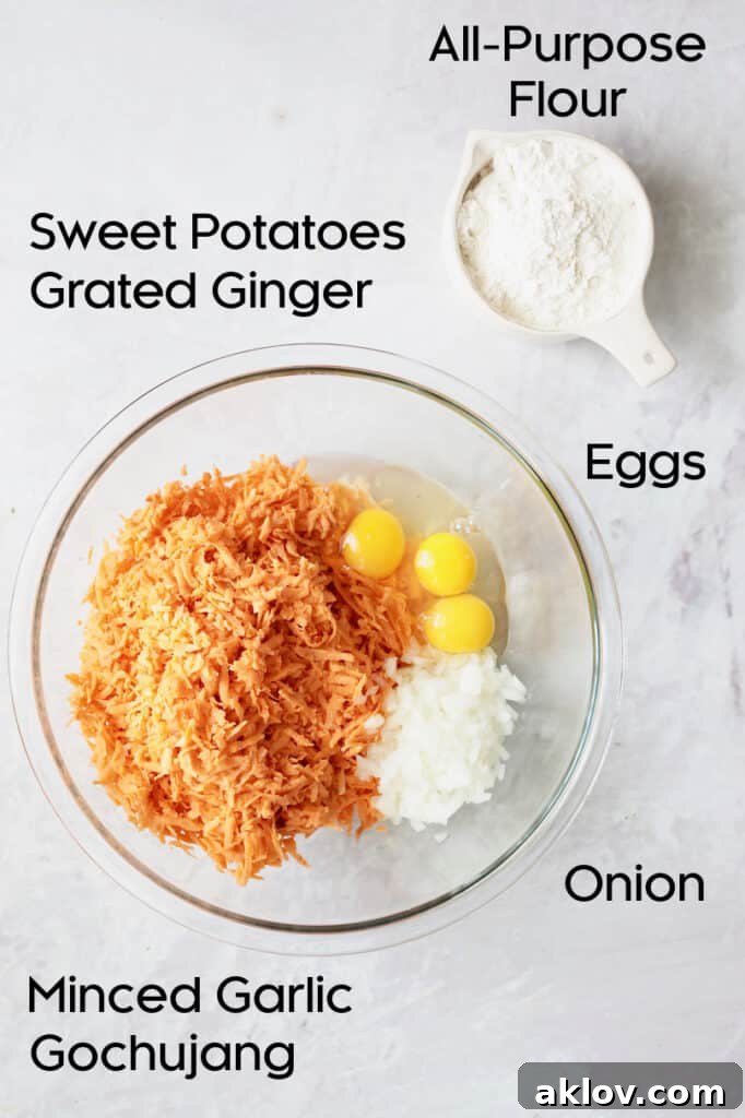 All the raw ingredients for Korean Sweet Potato Fritters laid out, including grated sweet potatoes, chopped onion, garlic, ginger, eggs, flour, and gochujang.