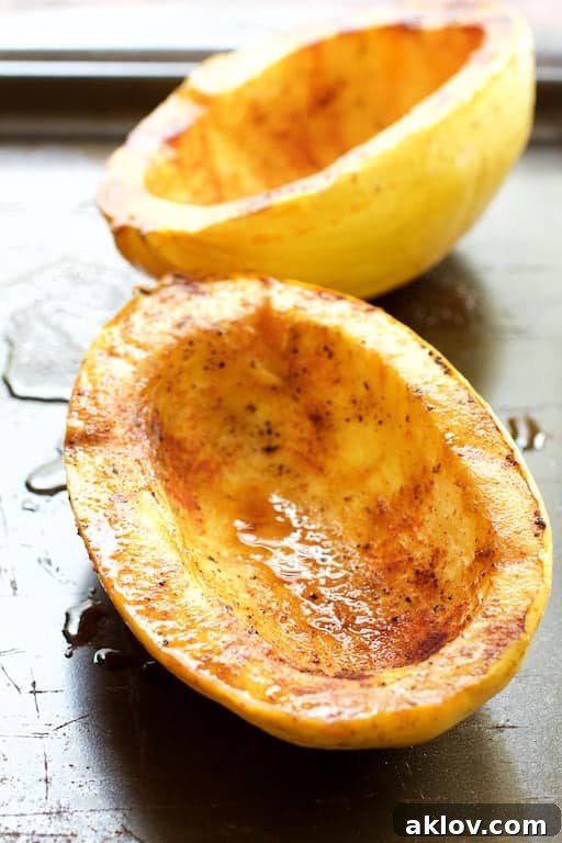 Two halves of roasted spaghetti squash, golden-brown and steaming, resting on a baking sheet, ready to be shredded into pasta-like strands.
