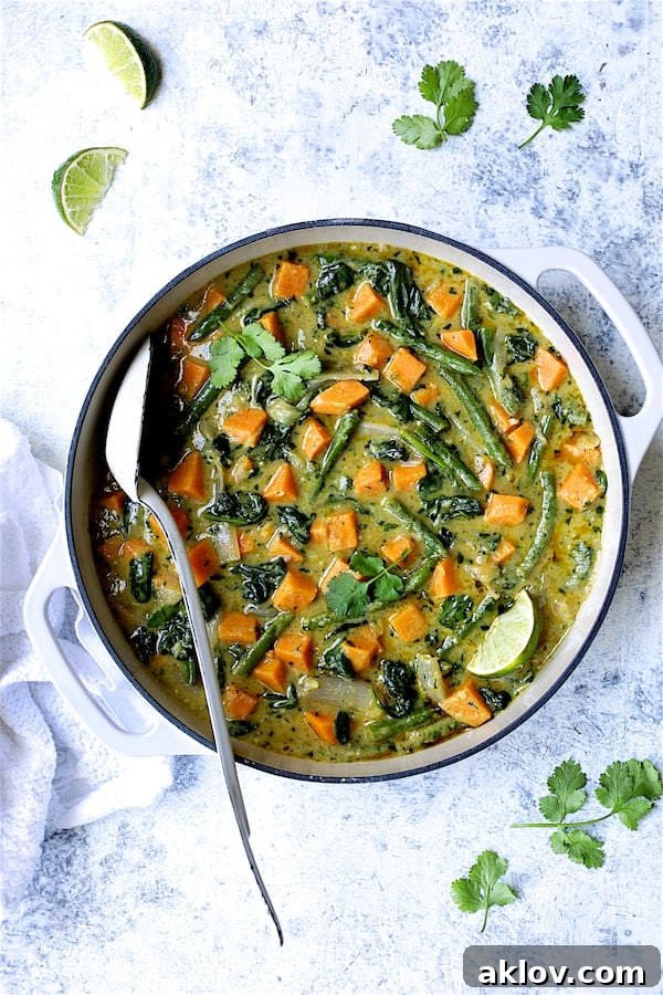 Photo of Vegan Thai Green Sweet Potato Curry on pale blue background garnished with cilantro and lime wedges.