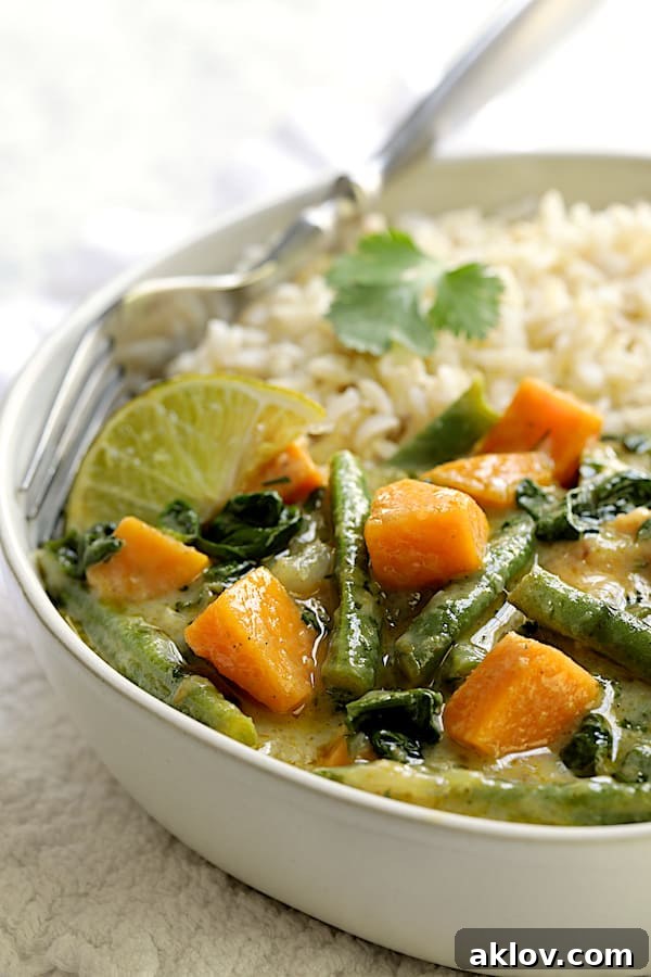 Close-up photo of Vegan Thai Green Sweet Potato Curry in white bowl with rice and fork.