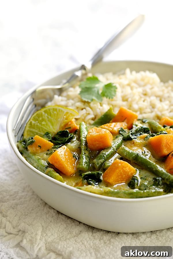 Photo of a bowl of Vegan Thai Green Sweet Potato Curry with rice on white fabric.