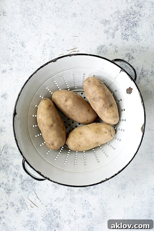 Golden Garlic Herb Potato Galettes in a Muffin Tin 3 Four unpeeled Russet potatoes resting in an antique white colander, ready for preparation.