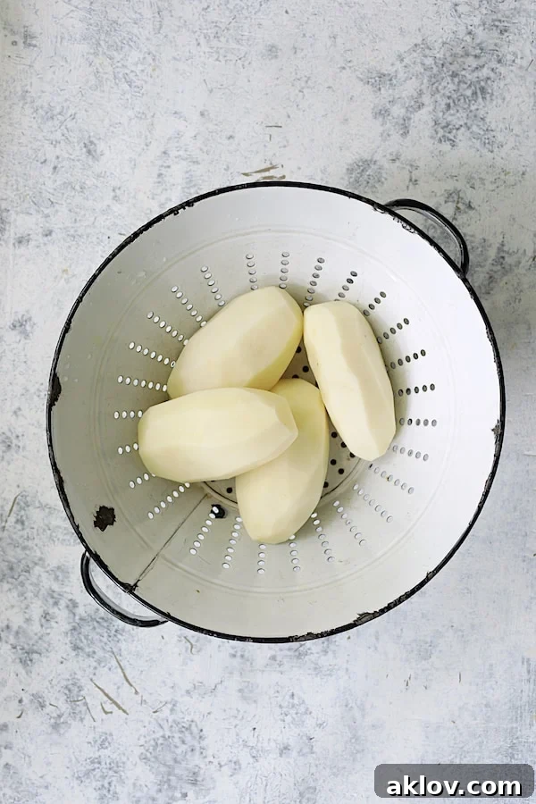 Golden Garlic Herb Potato Galettes in a Muffin Tin 4 Four peeled Russet potatoes neatly arranged in an antique white colander, ready for slicing.