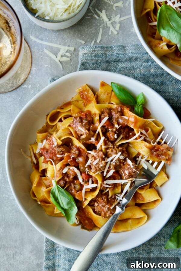 Slow Cooker Spicy Italian Sausage Ragu over pappardelle in white bowl garnished with fresh basil.
