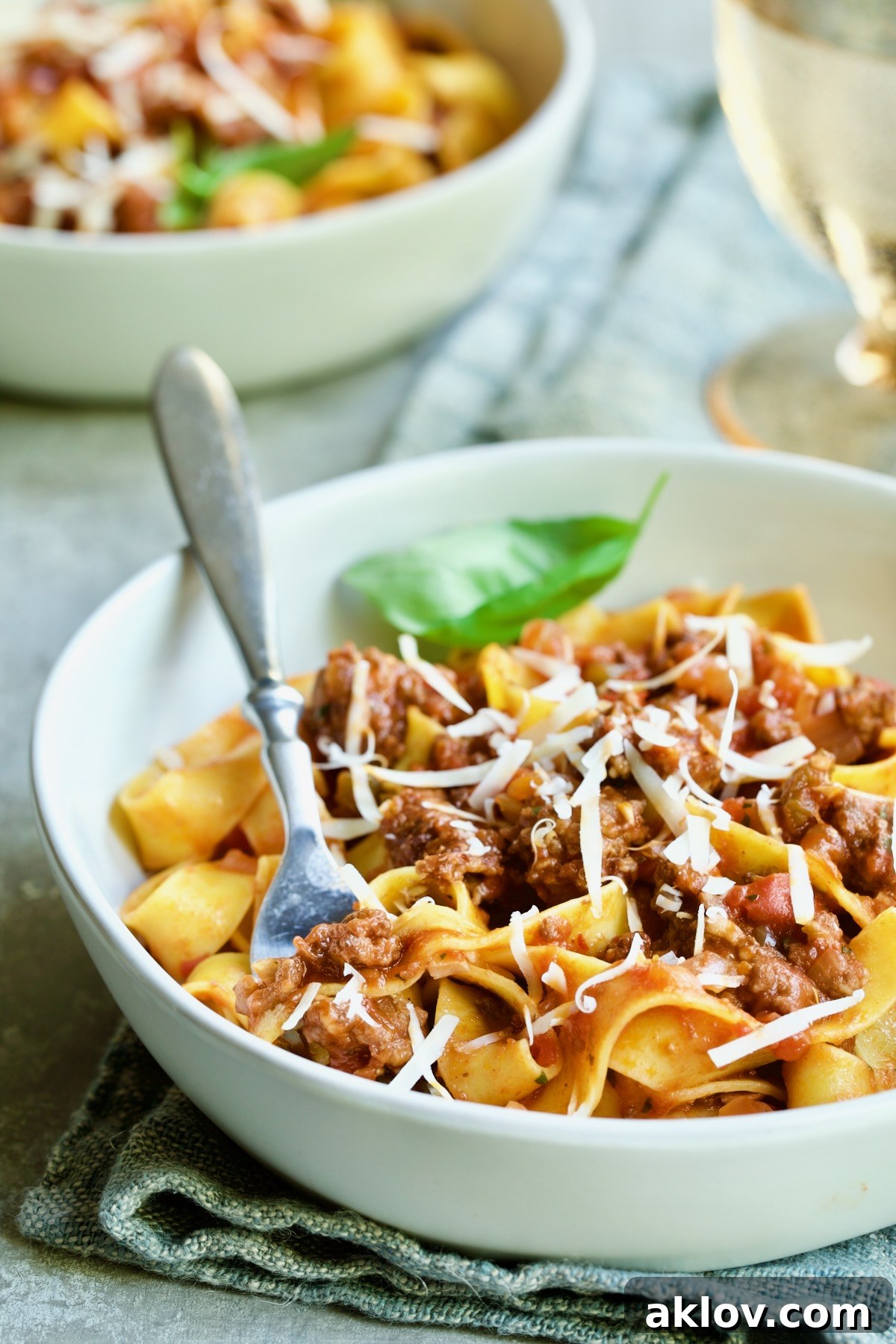 Slow Cooker Spicy Sausage and Pepper Ragu over pappardelle in white bowl with fork.