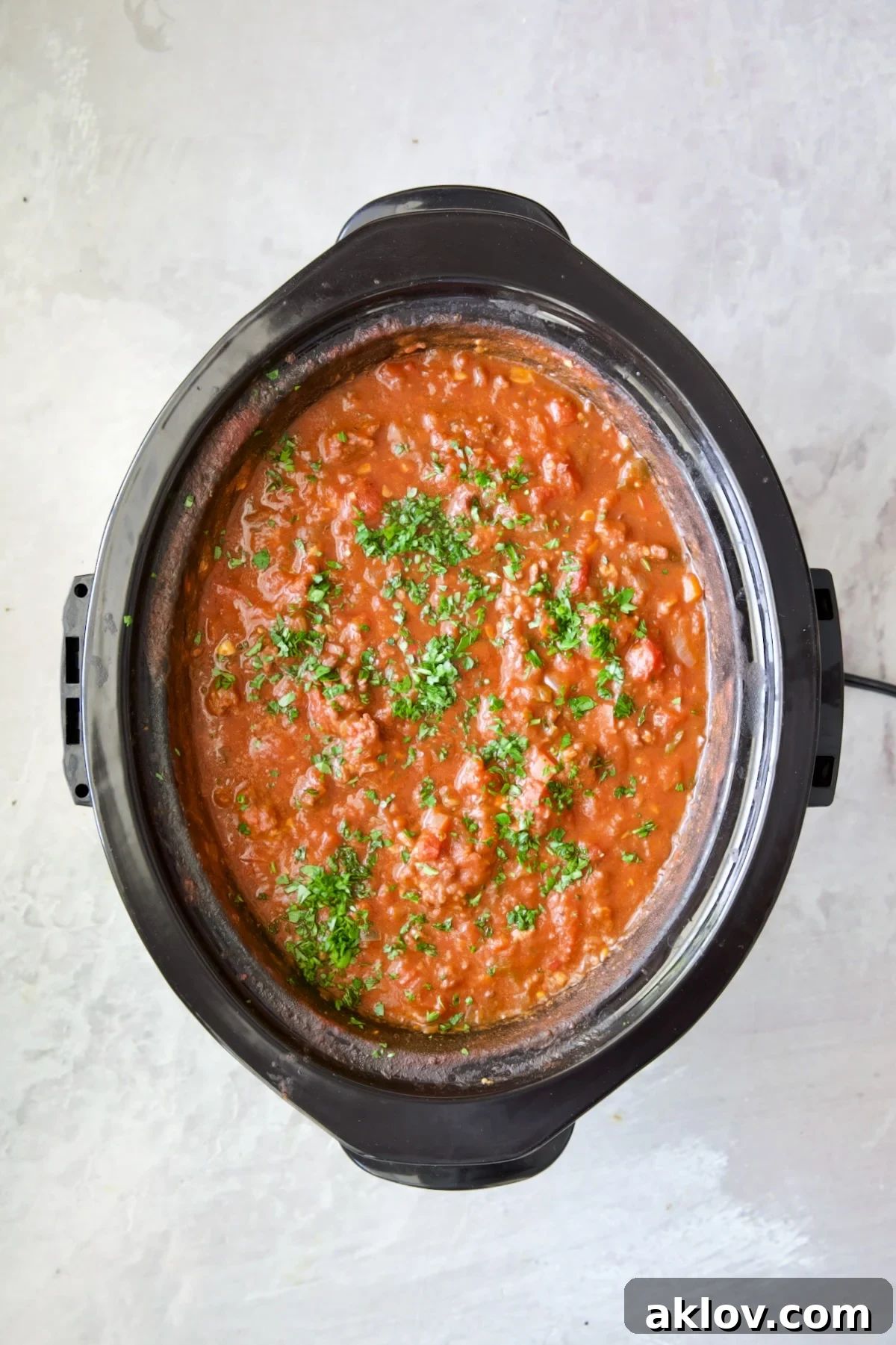 Slow Cooker Spicy Sausage and Pepper Ragu in slow cooker garnished with fresh parsley.