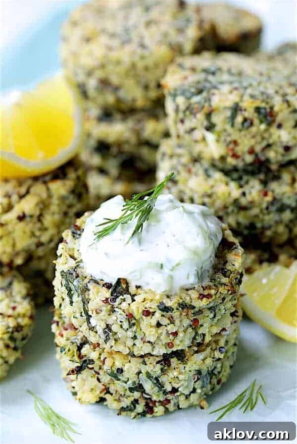 Two Greek Quinoa Cakes with Tzatziki stacked with tzatziki, garnished with lemon wedges and dill sprigs.