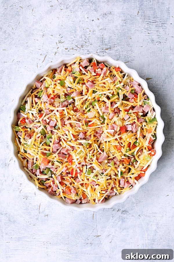 Photo of peppers, ham and cheese in round white baking dish before custard is poured in.