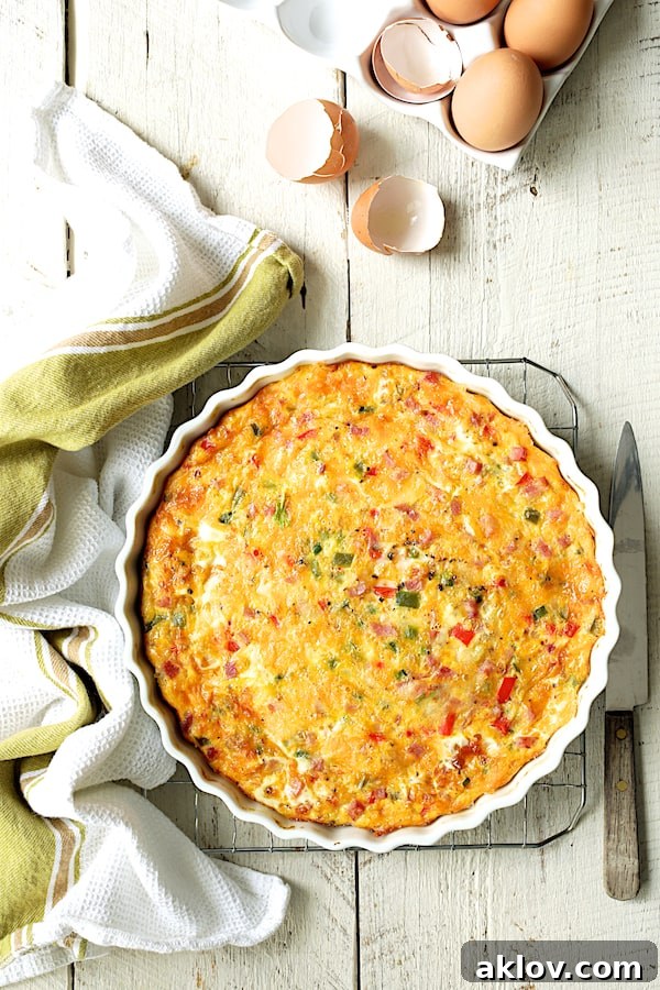Photo of cooked Spicy Baked Denver Omelet on cooling rack with green striped towel and egg shells nearby.