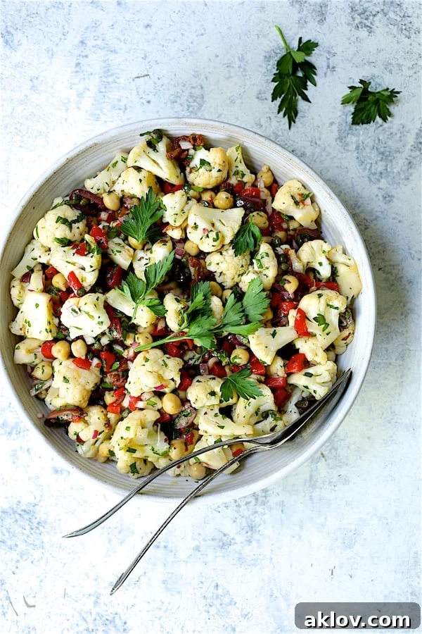 Photo of Sicilian Cauliflower Salad in white serving bowl with serving utensils garnished with parsley sprigs.