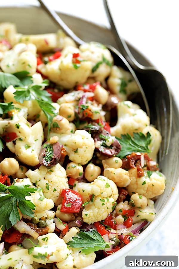Close-up photo of Sicilian Cauliflower Salad in white serving bowl with serving utensils.
