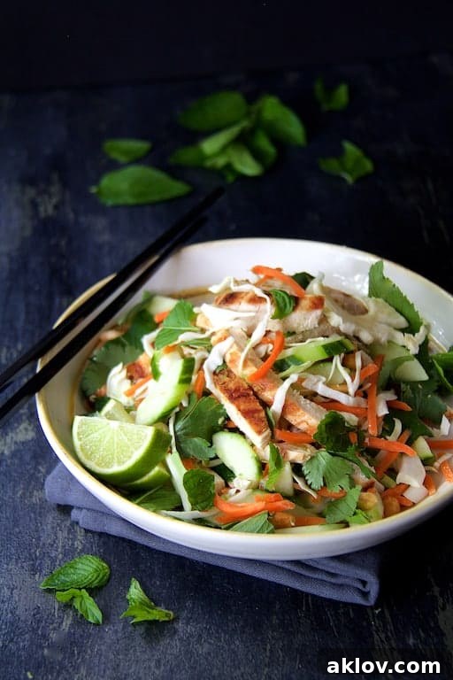 Vietnamese Chicken Salad with Spicy Lime Ginger Dressing in white bowl with black chopsticks set on blue napkin garnished with fresh mint leaves.
