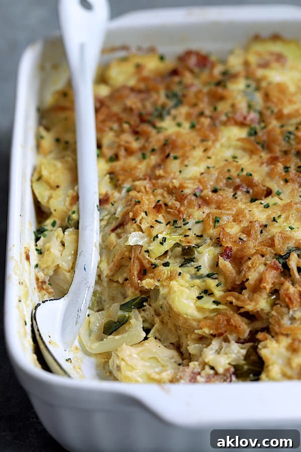 A generous portion of Potato Cabbage Casserole with Cheddar and Bacon in a white baking dish, with a serving spoon resting beside it.