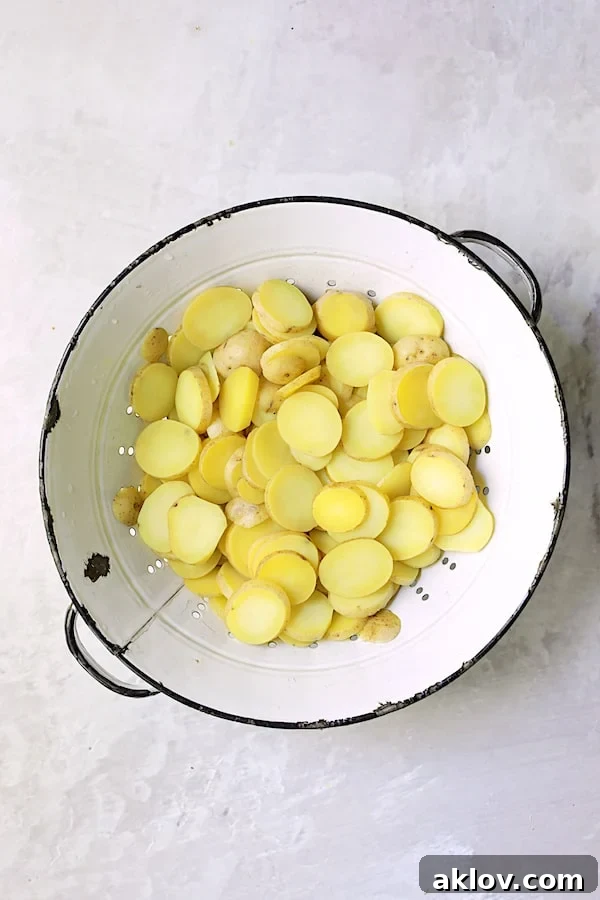 Sliced and par-cooked baby Yukon Gold potatoes cooling in a vintage white colander, showing their delicate texture.