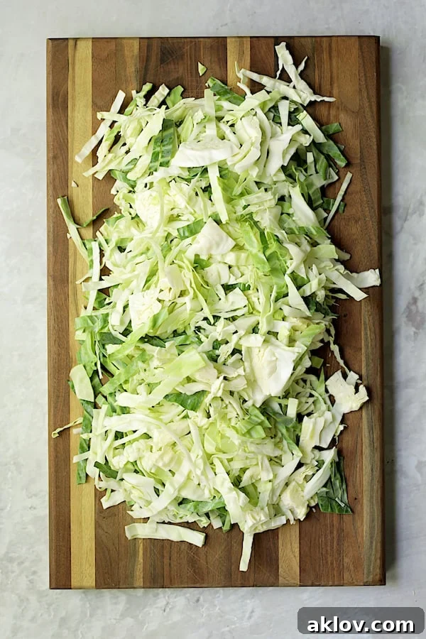 Freshly thinly sliced green cabbage spread out on a wooden cutting board, ready for cooking.