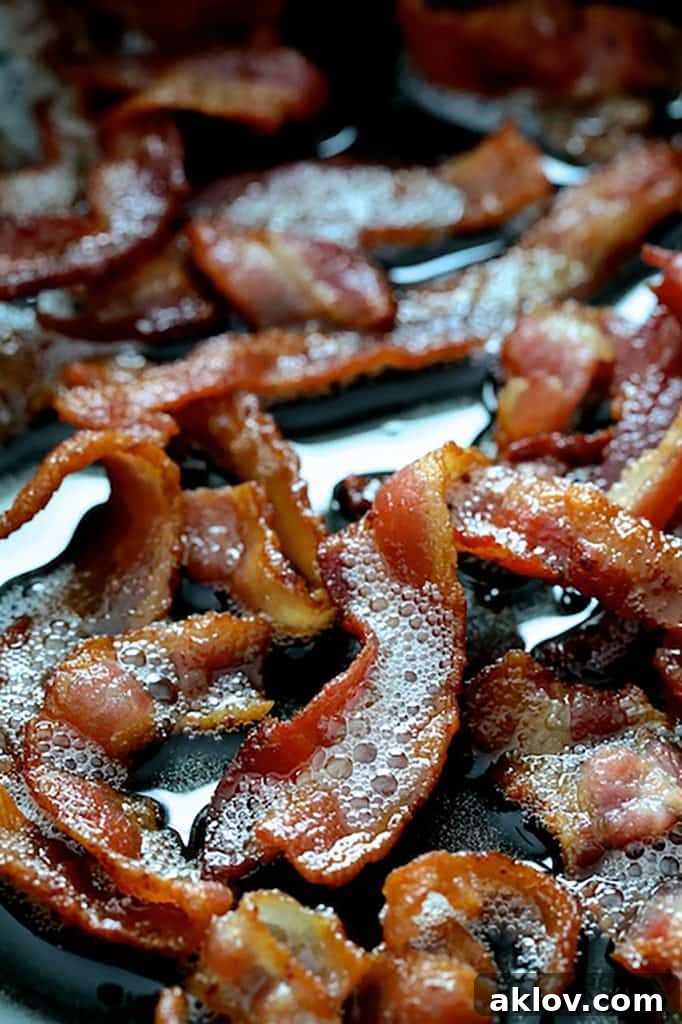 Crispy bacon sizzling in a skillet, showcasing the golden-brown texture, with rendered fat.